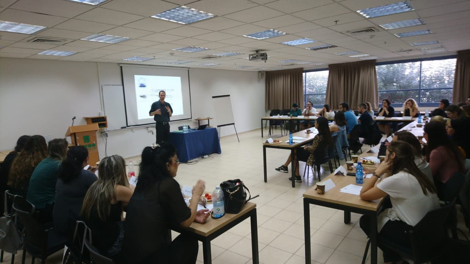 Presenter speaks to a seated audience in a classroom during a professional seminar.